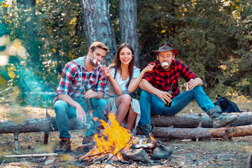 Young couples having picnic in woods. Young people having a camping. Company friends enjoy relaxing together in forest. Hikers sharing impression of walk and eating. Summer vacation forest.