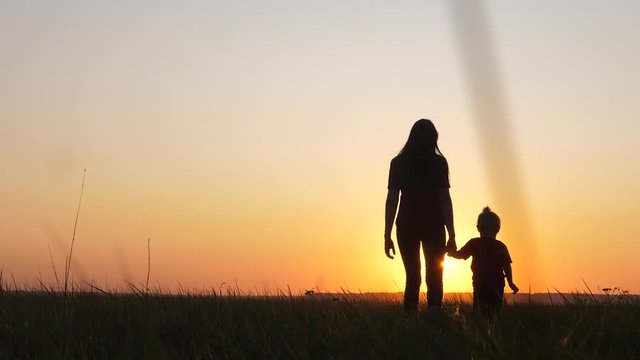 happy family a mom and daughter sunset silhouette in the park walking go slow motion. little girl and woman mom lifestyle hold hand walk go the field outdoors. happy family mom takes care of daughter