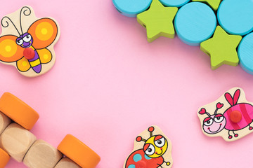 Top view on children's educational toys, multi-colored cubes, stars,circles on a pink background. Cute butterfly, ladybug, bee, wooden train. Flat lay, copy space for text.