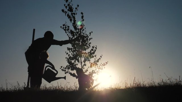 happy family of farmers a silhouette concept slow motion video. dad son and daughter children plant and water the tree outdoors in the park. happy family little girl and boy works lifestyle in garden