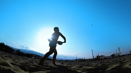 Silhouette of young men play ball paddle beach or tennis on the sand in the shore of the beach