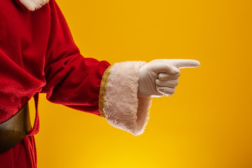 Photo of Santa Claus gloved hand in pointing gesture. Santa Claus pointing his fingers over yellow....