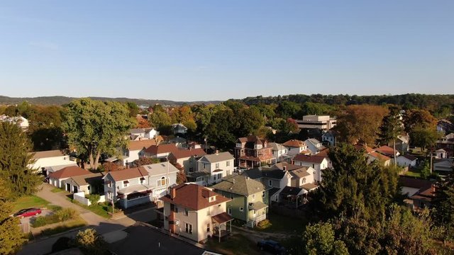 An early evening rising aerial establishing shot of an upscale residential neighborhood in the Pennsylvania hills. Pittsburgh suburbs. Ohio River in the far distance.  	