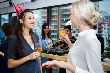Group of happy colleagues having fun at a new year celebration ahead. Business people with diverse ethnicities are smiling, dancing, laughing and drinking wine or champagne in the modern office.