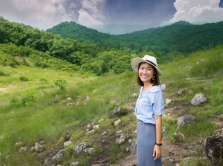 Naklejka premium Asian young woman in casual clothes wearing a white hat is standing among nature, mountains, and trees. A weekend trip to relax.