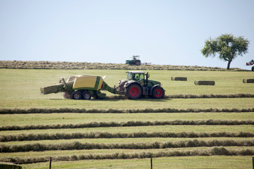 Traktor mit Anhänger auf der Wiese erntet Heu und presst Ballen	