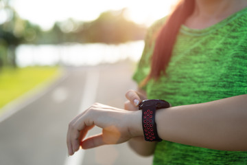 Young fitness woman runner setting up smart watch before running training during sunset. Outdoor exercise activities concept.