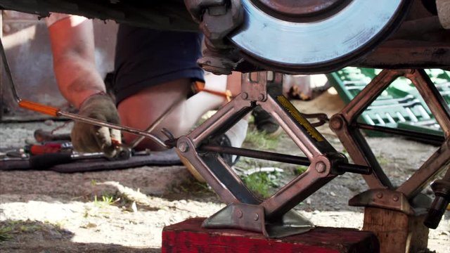 Close view of two tire jacks and mechanic turning a handle of it