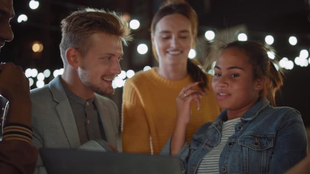 Beautiful and Handsome Friends are Using a Laptop Computer while Standing at a Table in an Outdoors Street Food Cafe. They're Watching a Video or an Online Stream. They are Happy and Smile.