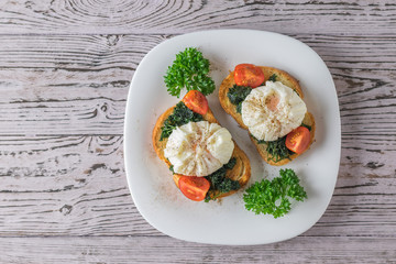 Poached eggs on toasted bread with herbs in a white plate. The view from the top.