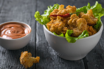 Baked cauliflower inflorescences with hot pepper and lettuce leaves in a white bowl.