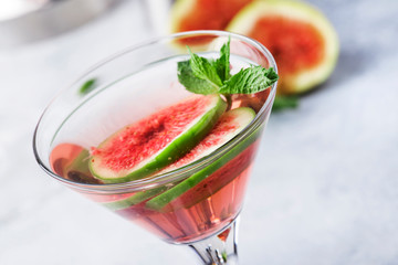 Pink fig martini alcoholic cocktail in shot glass on gray table with bar tools, copy space
