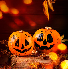 Halloween festive composition with smiling pumpkins guards with lights, lantern, straw and fallen leaves on dark wooden background, rustic style, selective focus