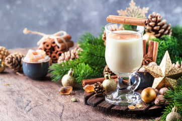 Christmas or New Year Eggnog alcoholic cocktail - hot winter drink with milk, eggs and rum, sprinkled with cinnamon and nutmeg in glass on gray background, copy space