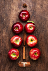 Creative Christmas tree made from red apples, cinnamon and anise star on wooden brown background