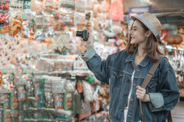 Smiling woman traveler in chiangmai market landmark chiangmai thailand holding camera with backpack on holiday, relaxation concept, travel concept