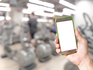 hand holding mobile smart phone with blur fitness gym equipment background