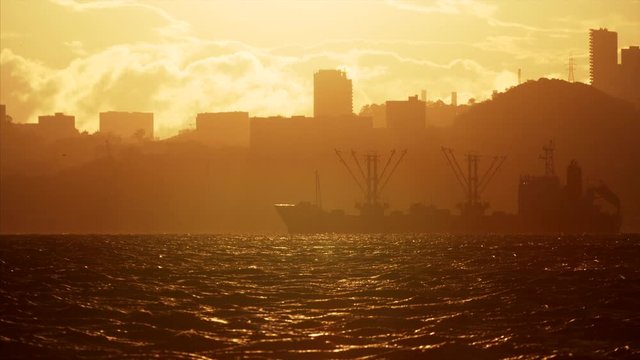 Silhouette of ship moored in seaport of Vladivostok. View across the bay of seaport and cityscape of Vladivostok at bright yellow dawning. Russia