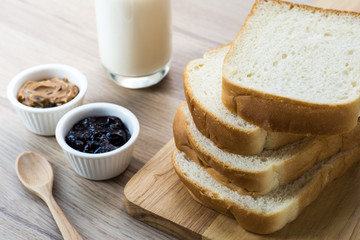 wooden board with Breakfast bread slices with milk on the wooden table. Black currant jam and Peanut butter in the small cup. Selective focus.