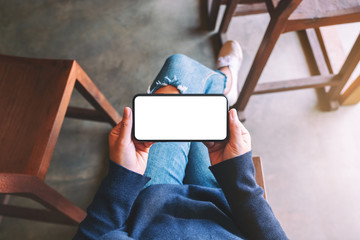 Top view mockup image of a woman holding black mobile phone with blank white screen while sitting in cafe
