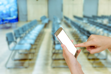 Woman using mobile smart phone with blurry chair in auditorium background