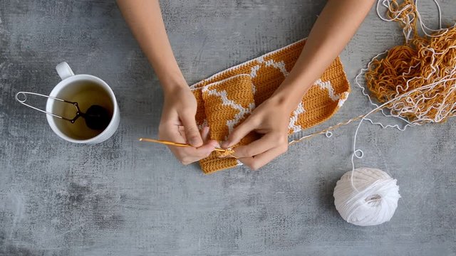 young womans hands crocheting with orange and white cotton thread on stone table background, top view close-up full HD stock video footage in real-time