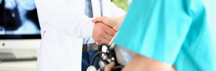Two doctors in office shaking hands celebrating successful treatment closeup