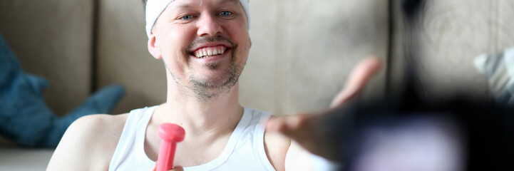 Male vlogger holds dumbbells in his hands and shouts at the camera on his subscriber, motivating them to action. Tutoring grade on an individual program online fraud concept aganist home background.