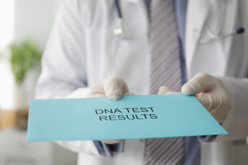 Male doctor hand holds out an envelope with results of genetic dna study. Paternity Test Concept