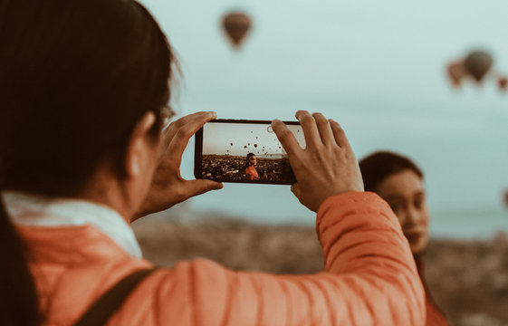 Woman taking a picture of a beautiful girlfriends with her smartphone against the Background of balloons in Cappadocia, Turkey