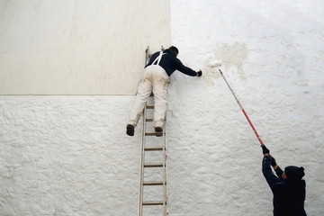 Workers painting facade while standing on the ladder