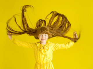 Beautiful happy red-haired girl in a yellow dress with fluttering up long hair on a yellow background