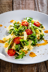 Pasta with tomatoes and arugula on wooden table
