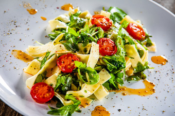 Pasta with tomatoes and arugula on wooden table