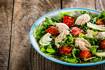 Salad with chicken meat and arugula on wooden table
