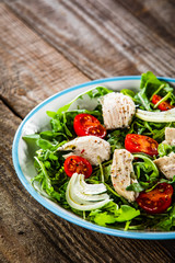 Salad with chicken meat and arugula on wooden table