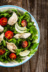 Salad with chicken meat and arugula on wooden table