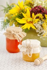 Glass jars with honey on the table and sunflowers in the background.