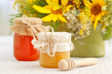 Glass jars with honey on the table and sunflowers in the background.