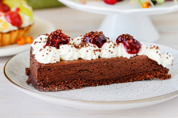 Chocolate cake with whipped cream decorated with cherries in a sweet sauce.