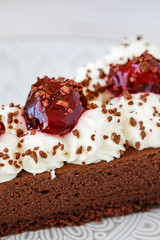 Chocolate cake with whipped cream decorated with cherries in a sweet sauce.