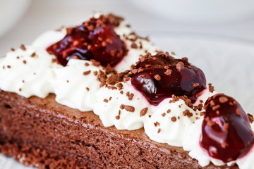 Chocolate cake with whipped cream decorated with cherries in a sweet sauce.