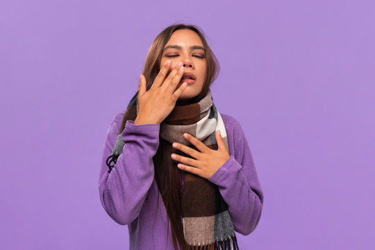 Pretty african-american girl in a sweater and cosy checked scarf sneezing standing isolated over purple background. Catching flu in winter.