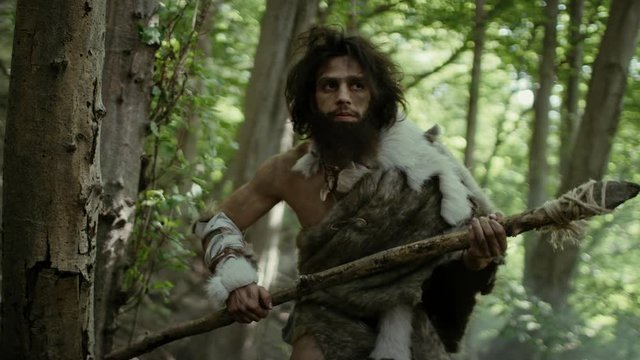 Portrait of Primeval Caveman Wearing Animal Skin and Fur Hunting with a Stone Tipped Spear in the Prehistoric Forest. Prehistoric Neanderthal Hunter Ready to Throw Spear in the Jungle