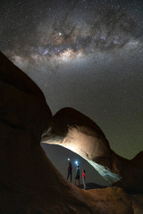 Group of people standing under milky way at Rock Arch Spitzkoppe, Namibia.
