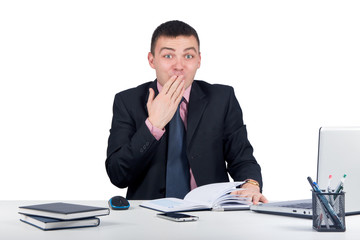 Young business man sitting at the office and looking shocked at the camera covering his mouth with his hand