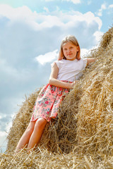 Naklejka na ściany i meble A girl with long flowing hair in a pink dress climbed on large bales of straw