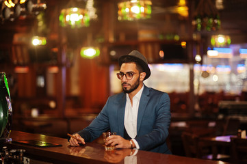 Handsome well-dressed arabian man with glass of whiskey and cigar posed at pub.