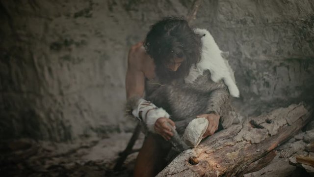 Primeval Caveman Wearing Animal Skin Holds Sharp Stone and Makes First Primitive Tool for Hunting Animal Prey, or to Handle Hides. Neanderthal Using Handax. Dawn of Human Civilization