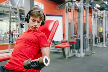 Fototapeta na wymiar cute young man in sports clothes and headphones is engaged with dumbbells in the gym
